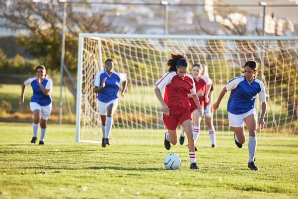 Teenage girls playing soccer on a grassy field during fall